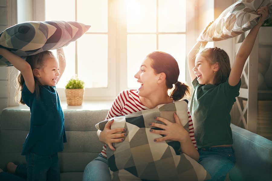 Blog - Mother and Children Having Fun During a Pillow Fight with Sunlight Shining Through Window in the Background