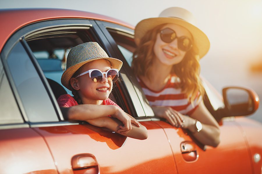 Personal Insurance - Two Children Laughing and Looking Outside of a Red Car at Sunset